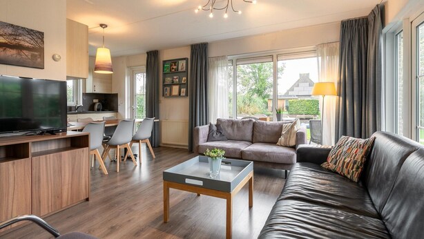 A modern living room with a sofa, coffee table, TV, and dining area. - Water villa with outdoor spa, jetty (Eernewoud)