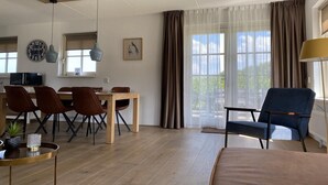 A modern living room with a dining area, wooden flooring, and a large window with curtains.