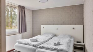 Ein Doppelbett mit weißer Bettwäsche und Kopfstütze, ein Nachttisch mit Lampe sowie ein Fenster mit Vorhängen.