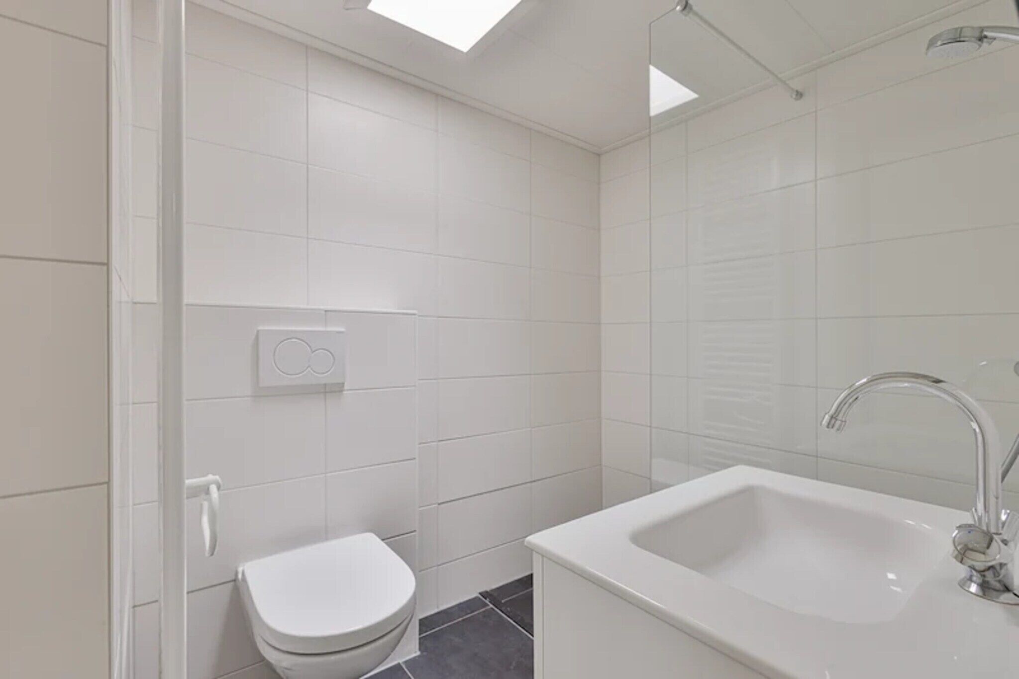 Een moderne badkamer met witte tegels, een toilet, een wastafel met spiegel en een douche.