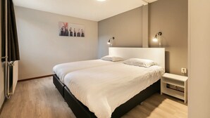 A bedroom with a large bed, a bedside table, a wall-mounted light, and a picture on the wall. - Cozy Forest Bungalow in the Veluwe (Kootwijk)