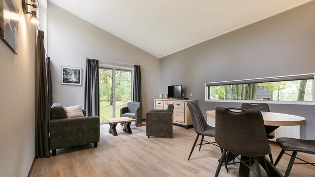 A modern room with a sofa, chairs, a dining table, and a TV. - Cozy Forest Bungalow in the Veluwe (Kootwijk)