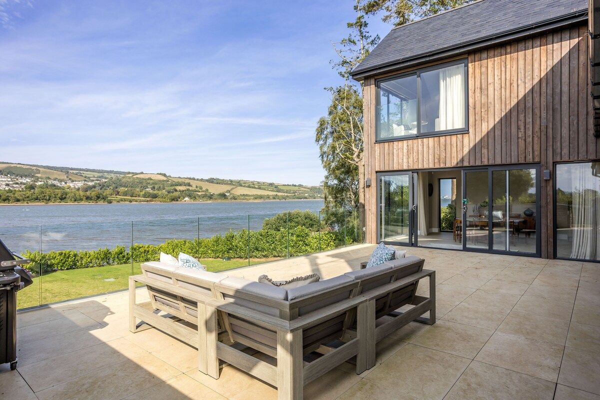 Une maison moderne dotée d’une grande terrasse offrant une vue sur un plan d’eau.