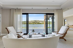 A modern living room with a large sliding glass door leading to a balcony with a view of a body of water and hills. - Gable View (Combeinteignhead)