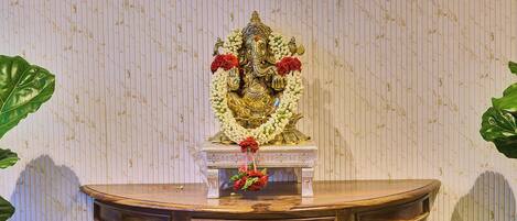 A wooden table with a statue on top, surrounded by green leaves.