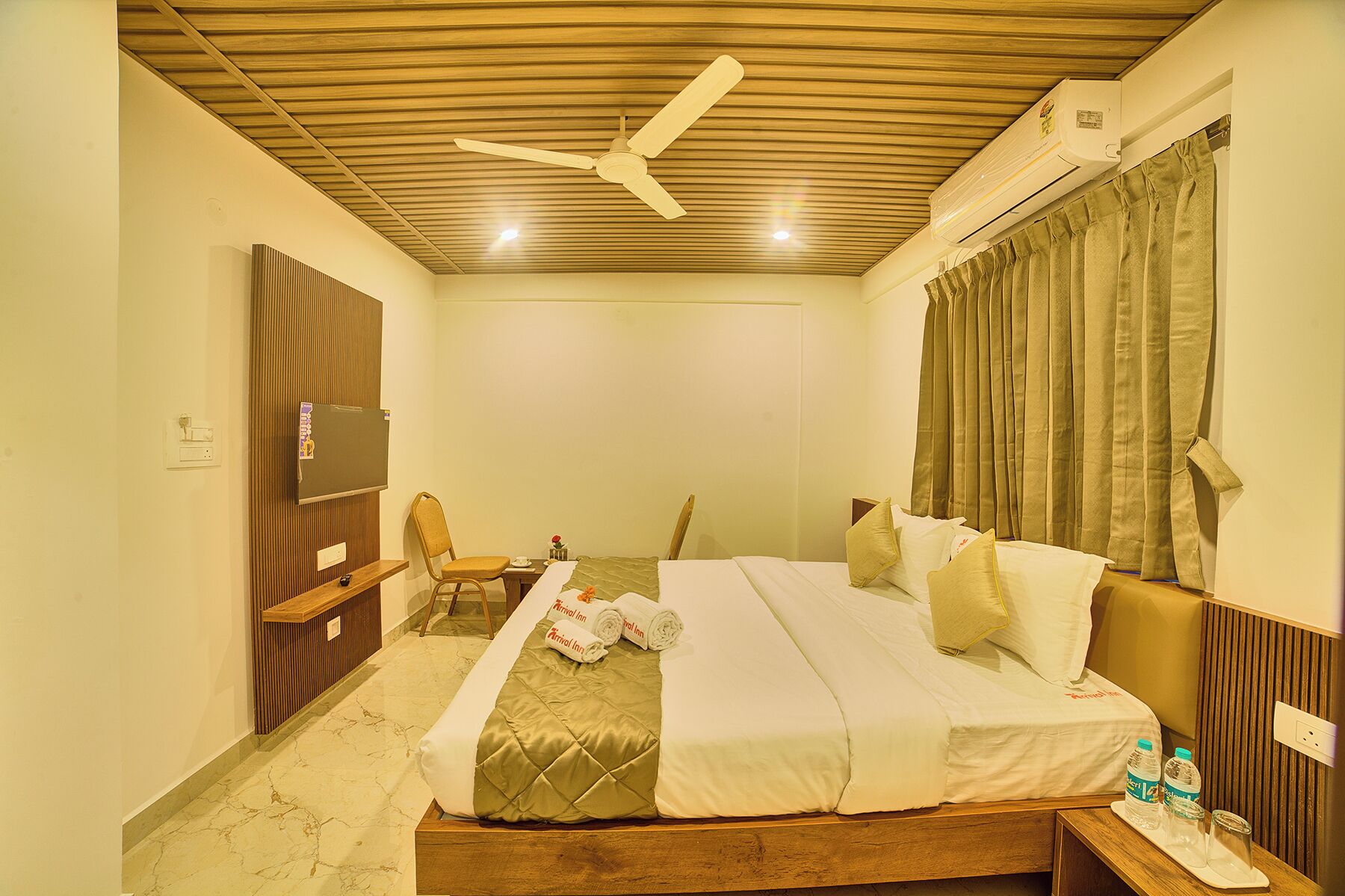 A hotel room with a wooden ceiling, a bed with white bedding, a chair, a small table, and a TV.