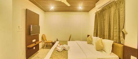 A hotel room with a wooden ceiling, a bed with white bedding, a chair, a small table, and a TV.