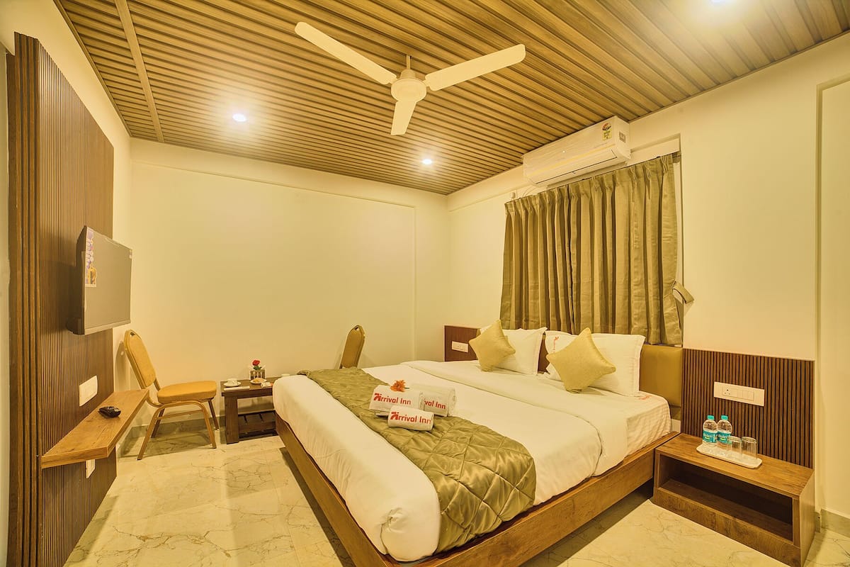 Ein Hotelzimmer mit Bett, Schreibtisch, Stuhl, Nachttisch, Deckenventilator und Klimaanlage.
