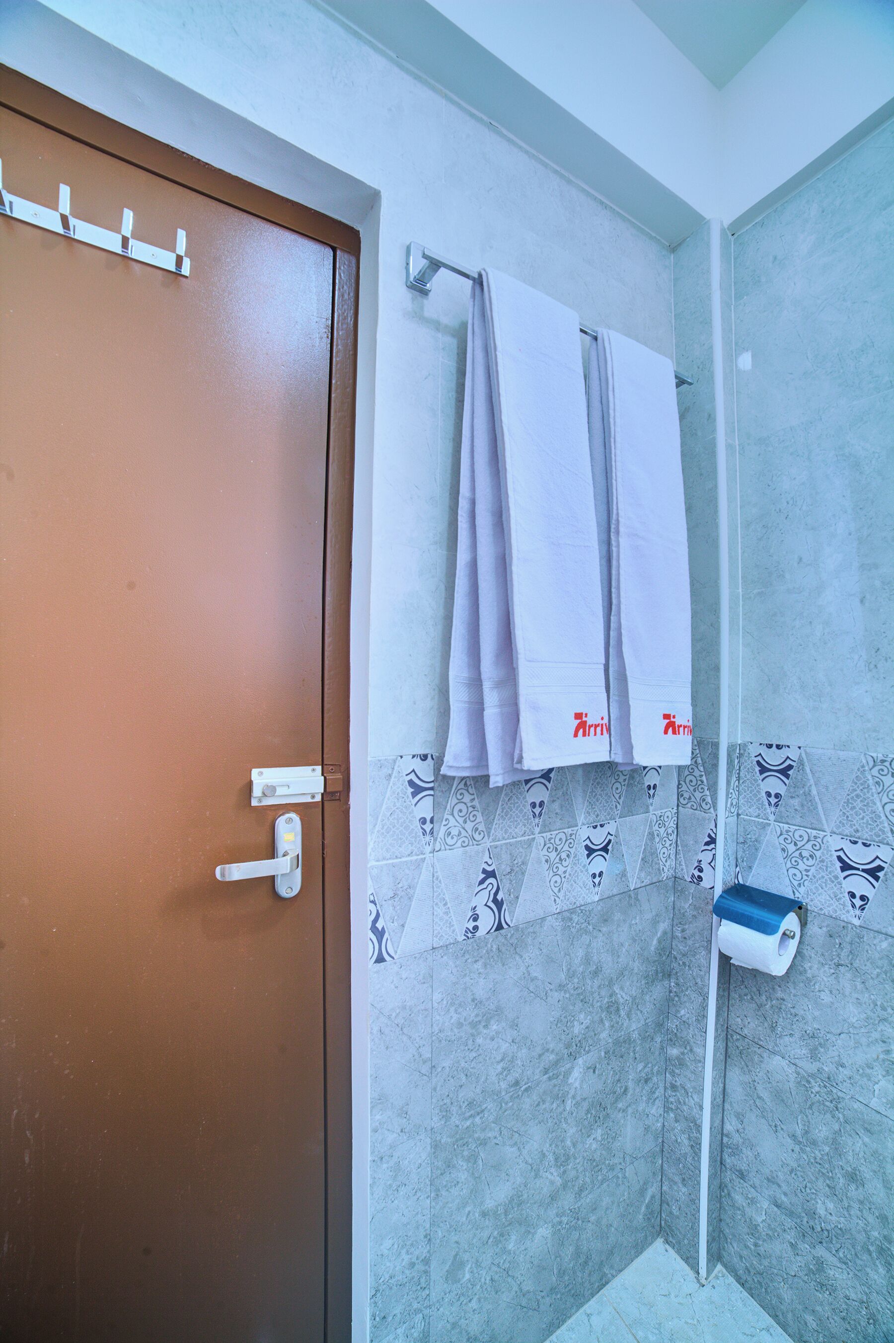 A bathroom with a brown door, a towel rack with two towels, a toilet paper holder, and patterned tiles.