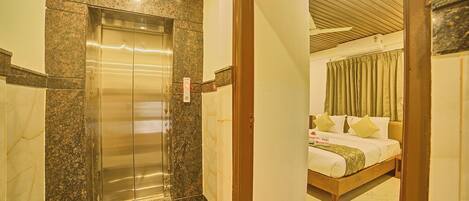 Una habitación de hotel con una cama, cabecera de madera y vista al pasillo.