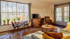 Un salon chaleureux avec un bureau en bois, une télévision et un canapé. De grandes fenêtres offrent une vue sur les arbres.