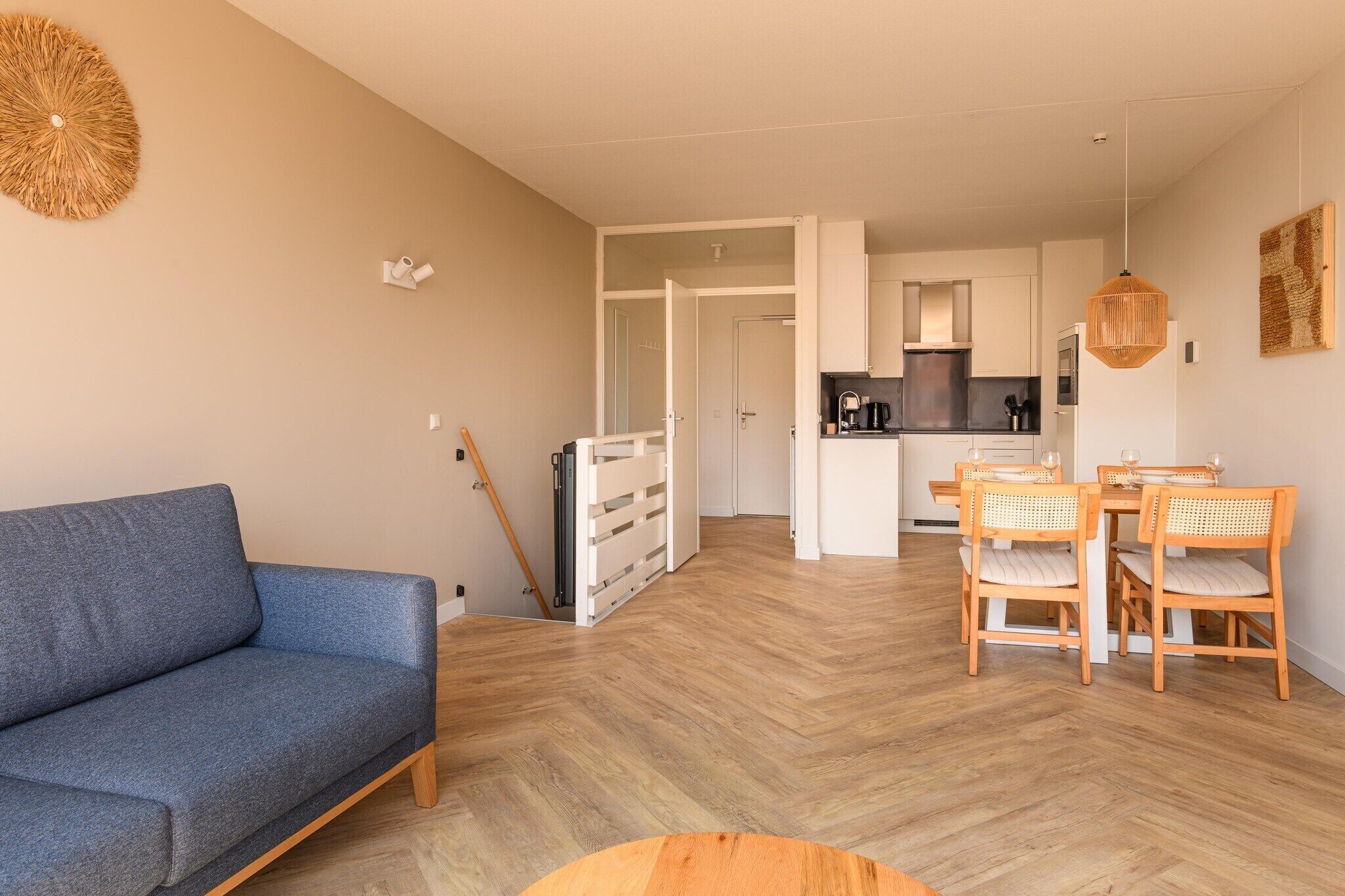 Un salon moderne avec un canapé, une table à manger et des chaises. On aperçoit une cuisine au fond.