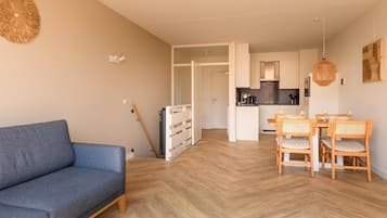 Un salon moderne avec un canapé, une table à manger et des chaises. On aperçoit une cuisine au fond.