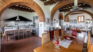 Une cuisine spacieuse avec des arches en briques, un coin repas avec une nappe à carreaux et un îlot central agrémenté d’un objet décoratif rouge.
