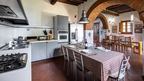 Une cuisine équipée d’appareils modernes, une table à manger pour quatre personnes et un plafond voûté en briques.