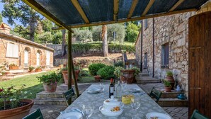 Un espace de restauration en plein air avec une table dressée pour deux personnes, entouré de plantes en pot et d’un mur de pierre.