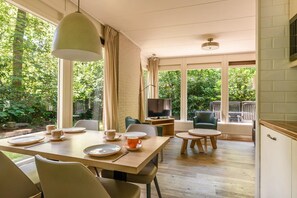 Un comedor con una mesa dispuesta para cuatro, un televisor y vistas al jardín.