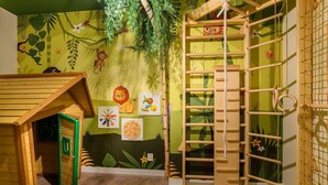 A playroom with a wooden playhouse, climbing wall, and jungle-themed wall decorations. - Jungle-themed family escape (Bruinisse)