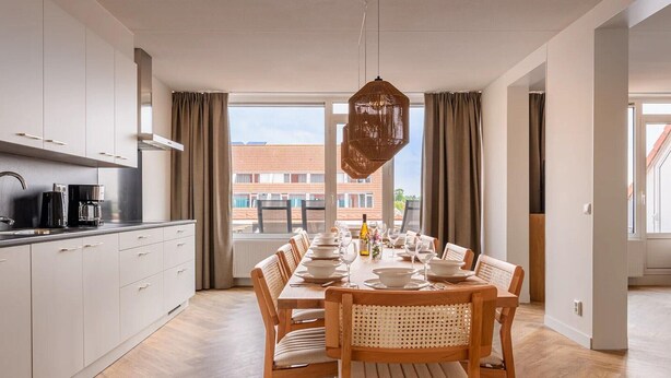 A modern kitchen with white cabinets and a dining area with a wooden table set for six. - Luxe 10-person family getaway (Bruinisse)