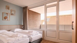 A hotel room with two beds, a large window, and a view of a building with a tiled roof. - Luxe 10-person family getaway (Bruinisse)
