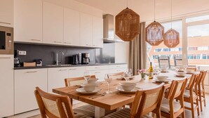 A modern kitchen with white cabinets, a wooden dining table set for six, and a large window offering a view of buildings. - Luxe 10-person family getaway (Bruinisse)