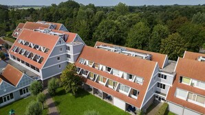 A multi-story hotel with a red-tiled roof, multiple balconies, and a courtyard with greenery. - Luxe 10-person family getaway (Bruinisse)
