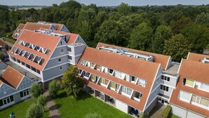 A multi-story hotel with a red-tiled roof, multiple balconies, and a courtyard with greenery. - Spacious comfort stay for couple (Bruinisse)