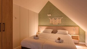 A bedroom with a sloped ceiling, a bed with white bedding, two bedside tables, and a wall-mounted light fixture. - Cosy apartment in Bruinisse with balcony (Bruinisse)