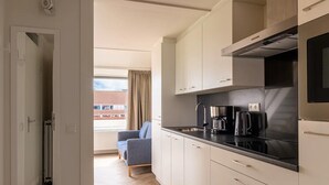 A modern kitchen with white cabinets, a black countertop, and a built-in stove. There is a window with curtains and a view of buildings outside. - Cosy apartment in Bruinisse with balcony (Bruinisse)