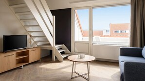 A modern room with a TV, wooden furniture, a small table, and a staircase leading to an upper level. - Cosy apartment in Bruinisse with balcony (Bruinisse)