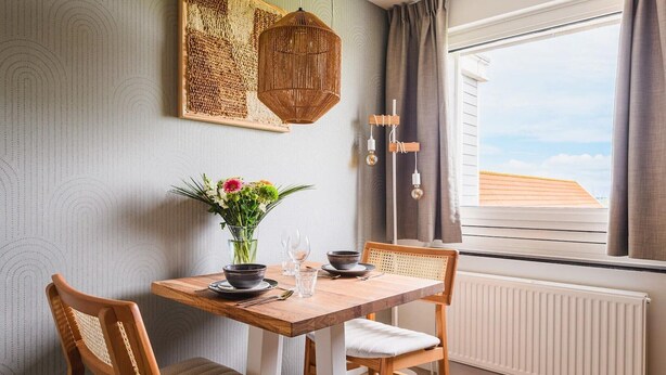A dining area with a wooden table, two chairs, a vase with flowers, and a hanging light fixture. - Cosy apartment in Bruinisse with balcony (Bruinisse)