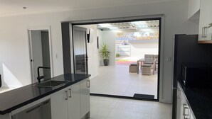 Una cocina moderna con encimera negra, electrodomésticos de acero inoxidable y una puerta corrediza de vidrio que da a un patio amoblado con mobiliario exterior y una planta en maceta.