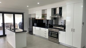 Una cocina moderna con armarios blancos, una isla central, electrodomésticos de acero inoxidable y vistas a un patio.