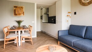 A modern living room with a dining table set for four, a sofa, and a kitchen in the background. - Modern apartment near centre facilities (Bruinisse)