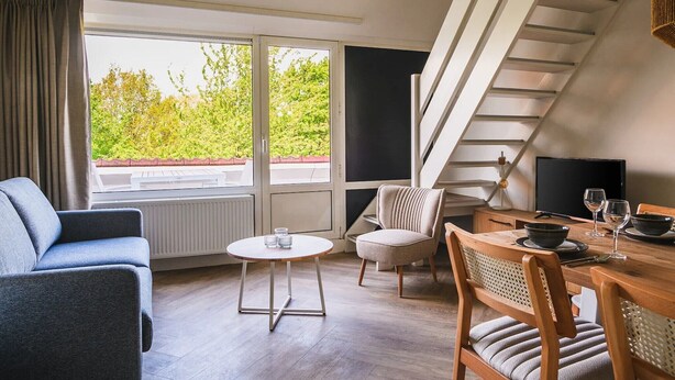 A modern living room with a sofa, chairs, a dining table, and a staircase. - Modern apartment near centre facilities (Bruinisse)