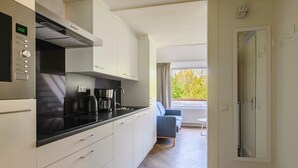 A modern kitchen with white cabinets, a black countertop, and a coffee maker. There is a window with curtains and a view of trees outside. - Modern apartment near centre facilities (Bruinisse)