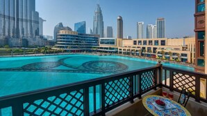 Una piscina con diseño geométrico, rodeada de edificios altos y un balcón con mesa y bebidas.