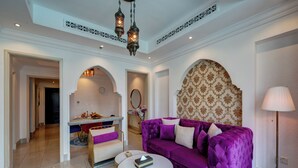 Un amplio salón con un sofá morado, una mesa de centro redonda y una zona de comedor con candelabro.
