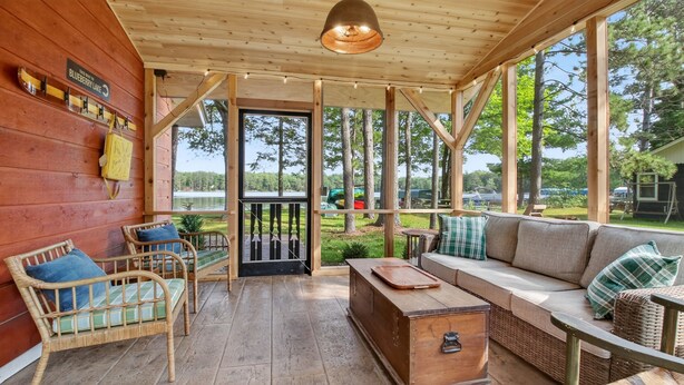 A wooden cabin with a porch, wicker furniture, and a view of the lake. - 4-Season Fun! Sandy Beach | Snowmobile Trails (Couderay)