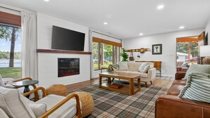 A modern living room with a fireplace, comfortable seating, and large windows offering a view of the outdoors. - 4-Season Fun! Sandy Beach | Snowmobile Trails (Couderay)