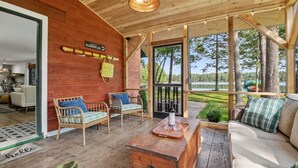A wooden cabin with a dining area, two wicker sofas, a wooden table with glasses, and a view of a lake. - 4-Season Fun! Sandy Beach | Snowmobile Trails (Couderay)
