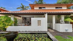A modern house with a tiled roof, a covered patio, a koi pond, and a statue.