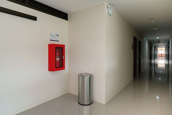 Un pasillo limpio y moderno con un extintor rojo montado en la pared, un contenedor de basura y un letrero con texto.