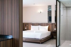 A modern hotel room with a large bed, a glass shower, and a wooden panel wall. - One Budget Hotel Chiangrai Bypass-West (Chiang Rai)