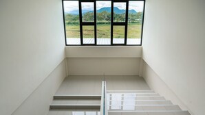Una scala conduce a un pianerottolo da cui si vede un prato e montagne attraverso una finestra.