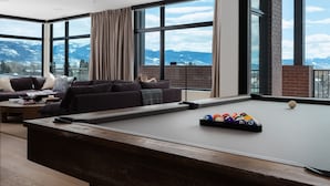 Un salon moderne avec une table de billard, de grandes fenêtres et une vue sur les montagnes.