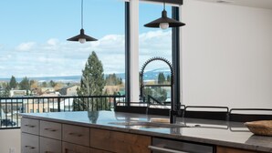 Une cuisine moderne dotée d’une grande fenêtre, de meubles en bois, d’un lave-vaisselle en acier inoxydable et de luminaires suspendus.