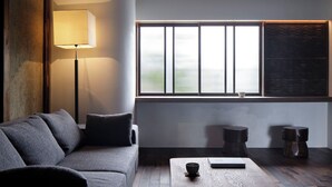 A modern living room with a sofa, a floor lamp, a table with a bowl and book, and a large window with blinds. - Renovated the main house of Maruyo Lumber, which is over 70 years old. Located in Funama-cho, Kuwana City, the site of the "Shichiri-no-watashi" ferry, the inn is a private house with antiques and artwork that blends the old and the new. (Semba cho, Kuwana city)