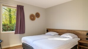 Un lit double avec une literie blanche, une tête de lit en bois, une table de chevet avec une lampe et deux assiettes décoratives fixées au mur.
