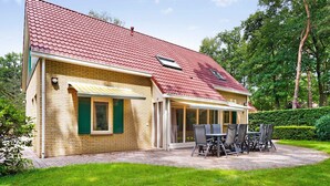 Une maison avec un toit recouvert de tuiles rouges, une façade en briques et un patio abrité avec une table et des chaises.